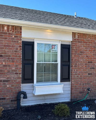 Brick house exterior with white window box and black shutters under clear blue sky.