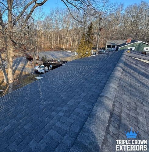 Aerial view of a new asphalt shingle roof on a residential home with trees in the background.