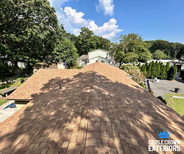 Aerial view of a recently shingled roof with trees and homes in the background.