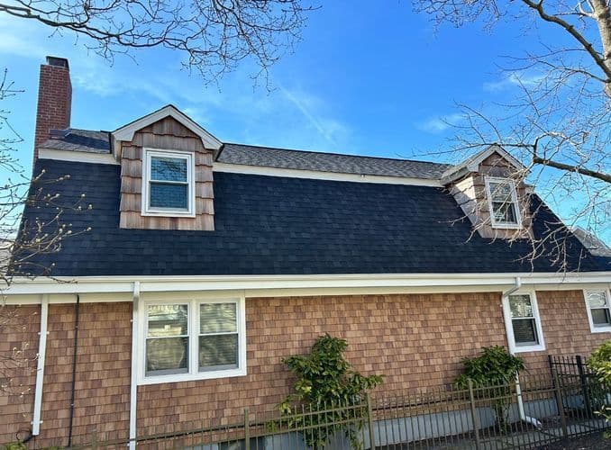 Cape Cod style house with shingle siding and dormer windows under a clear blue sky.