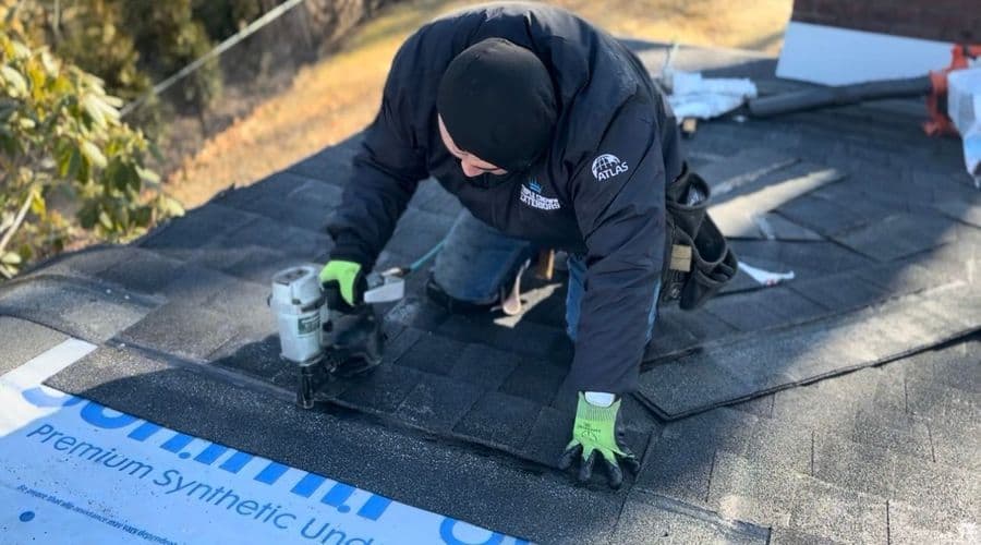 Roofer installing shingles on a roof, demonstrating roofing skills and safety gear.
