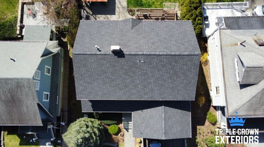Aerial view of a modern home with a newly installed dark shingle roof and landscaped yard.