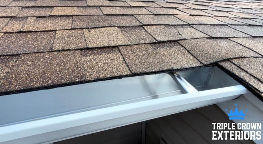 Close-up of a roof with shingle tiles and a nearby gutter installation by Triple Crown Exteriors.