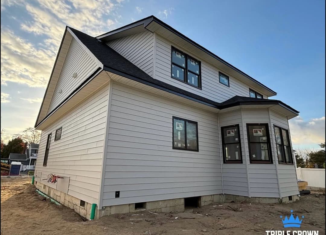 Newly built modern home with white siding and large windows under a clear sky.