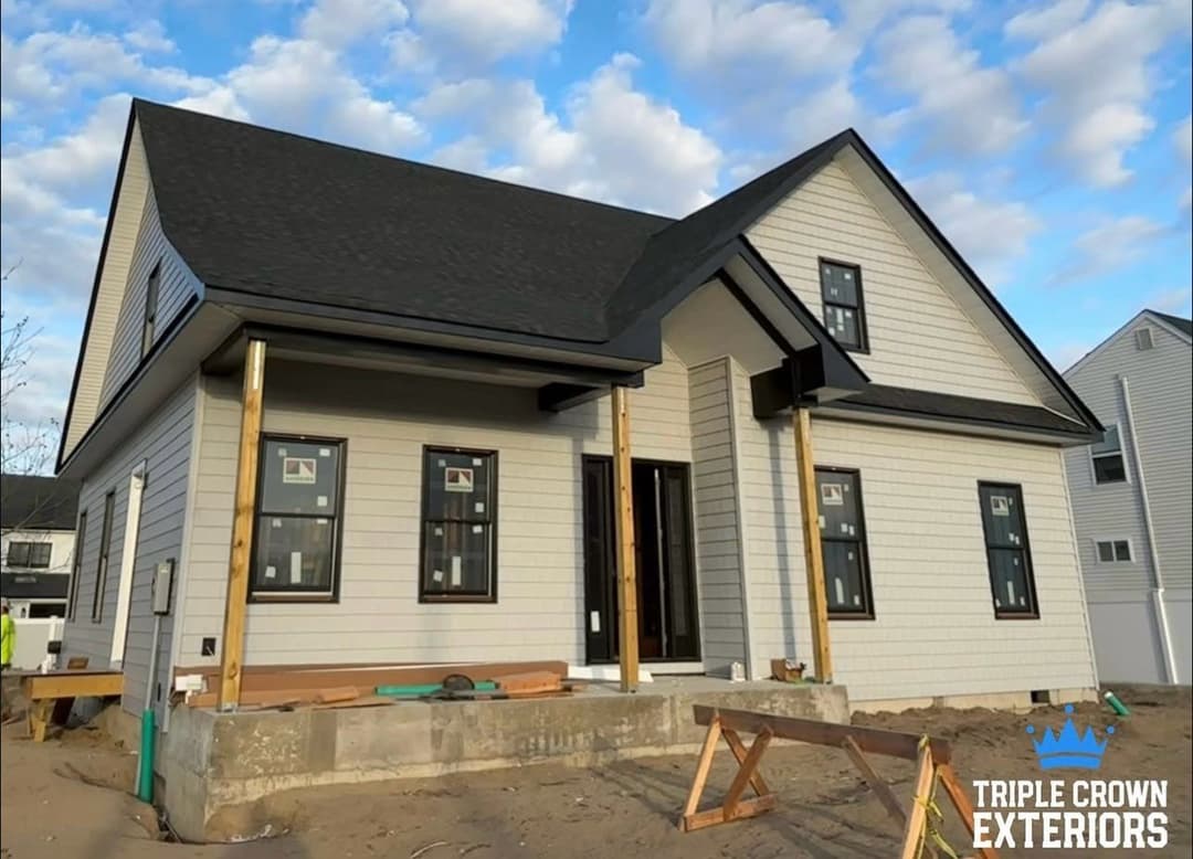 Newly constructed modern house with a black roof and white siding by Triple Crown Exteriors.