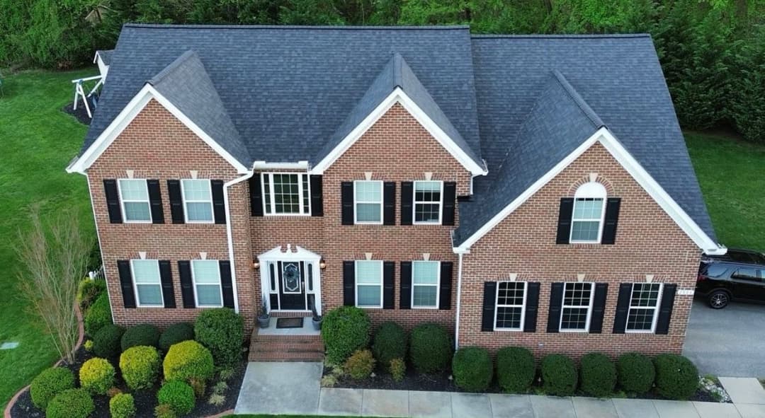 Aerial view of a two-story brick house with black shutters and landscaped yard.