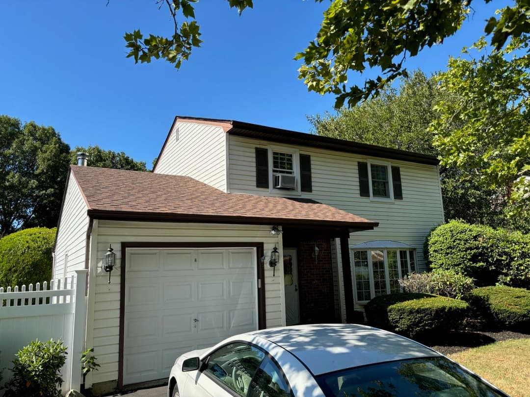 Two-story suburban house with white siding, brown roof, and green landscape.