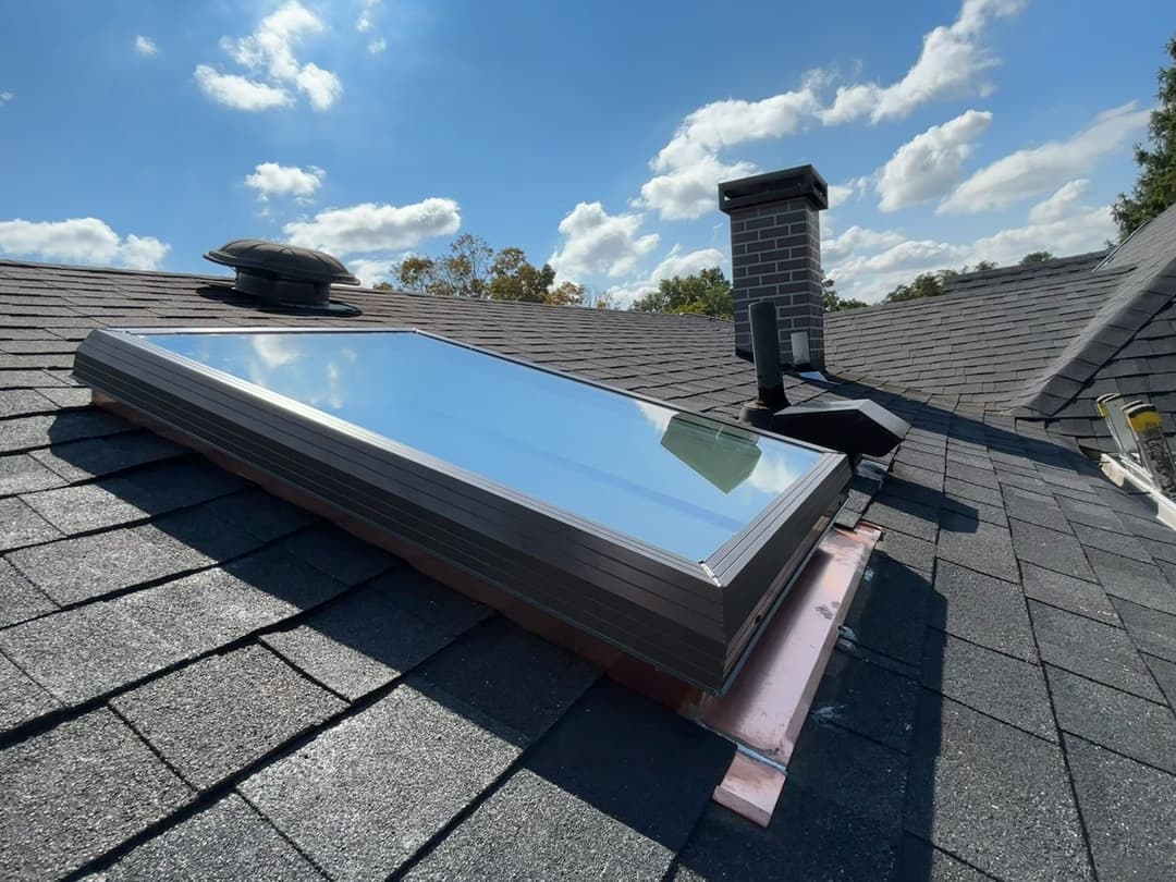 Modern skylight atop a sloped roof with chimney and clear blue sky in the background.