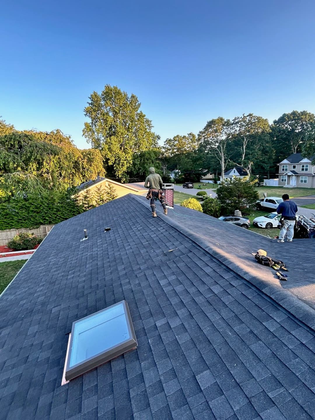 Roofer working on a residential roof with skylight, clear blue sky in background.