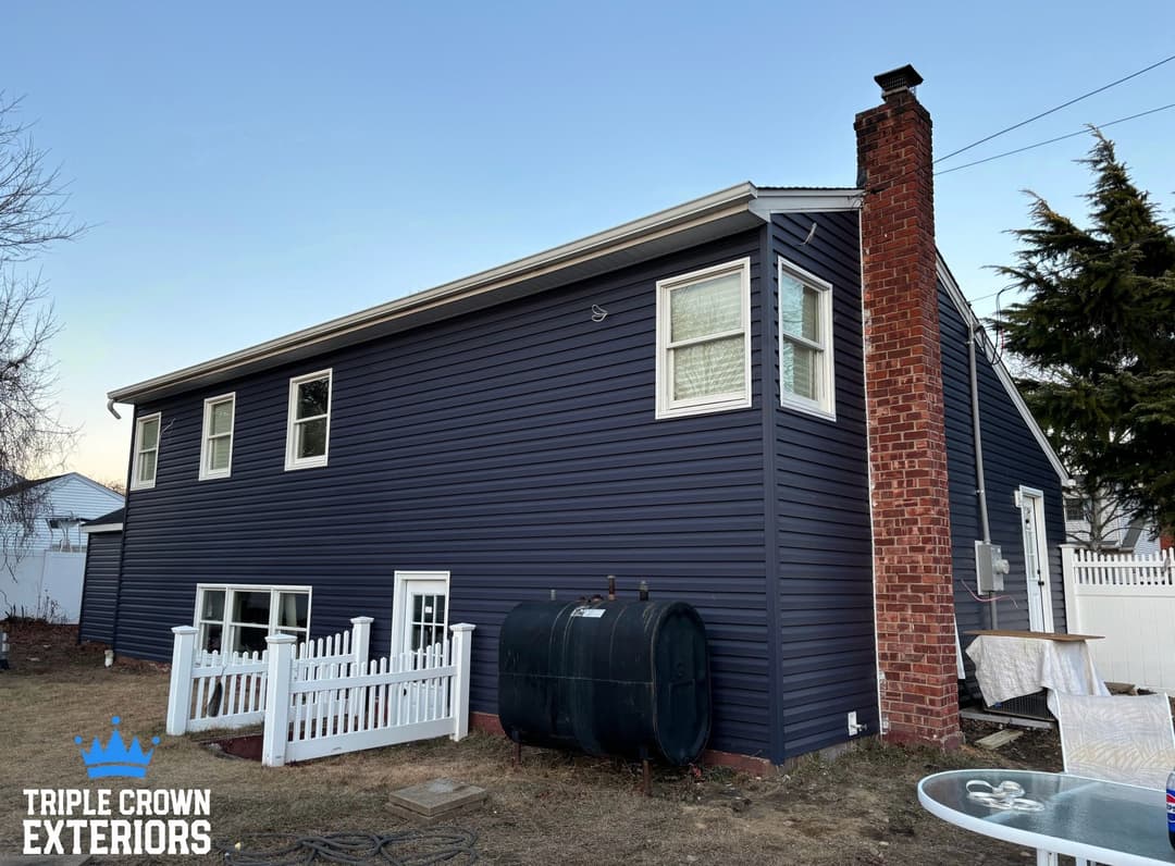 Modern blue vinyl siding on a house with a landscaped yard and white picket fence.