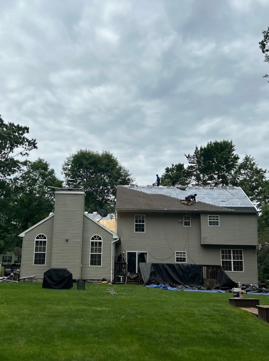 Roofers repairing a residential roof with cloudy sky in the background and green lawn below.