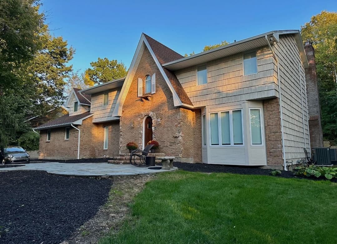 Modern brick home with large windows, stone pathway, and landscaped yard on sunny day.