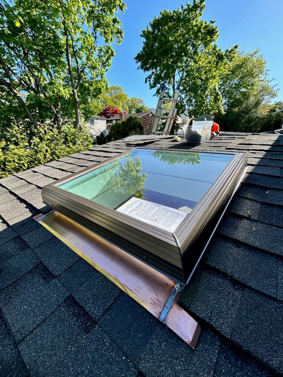Skylight installation on a shingled roof surrounded by greenery and trees.