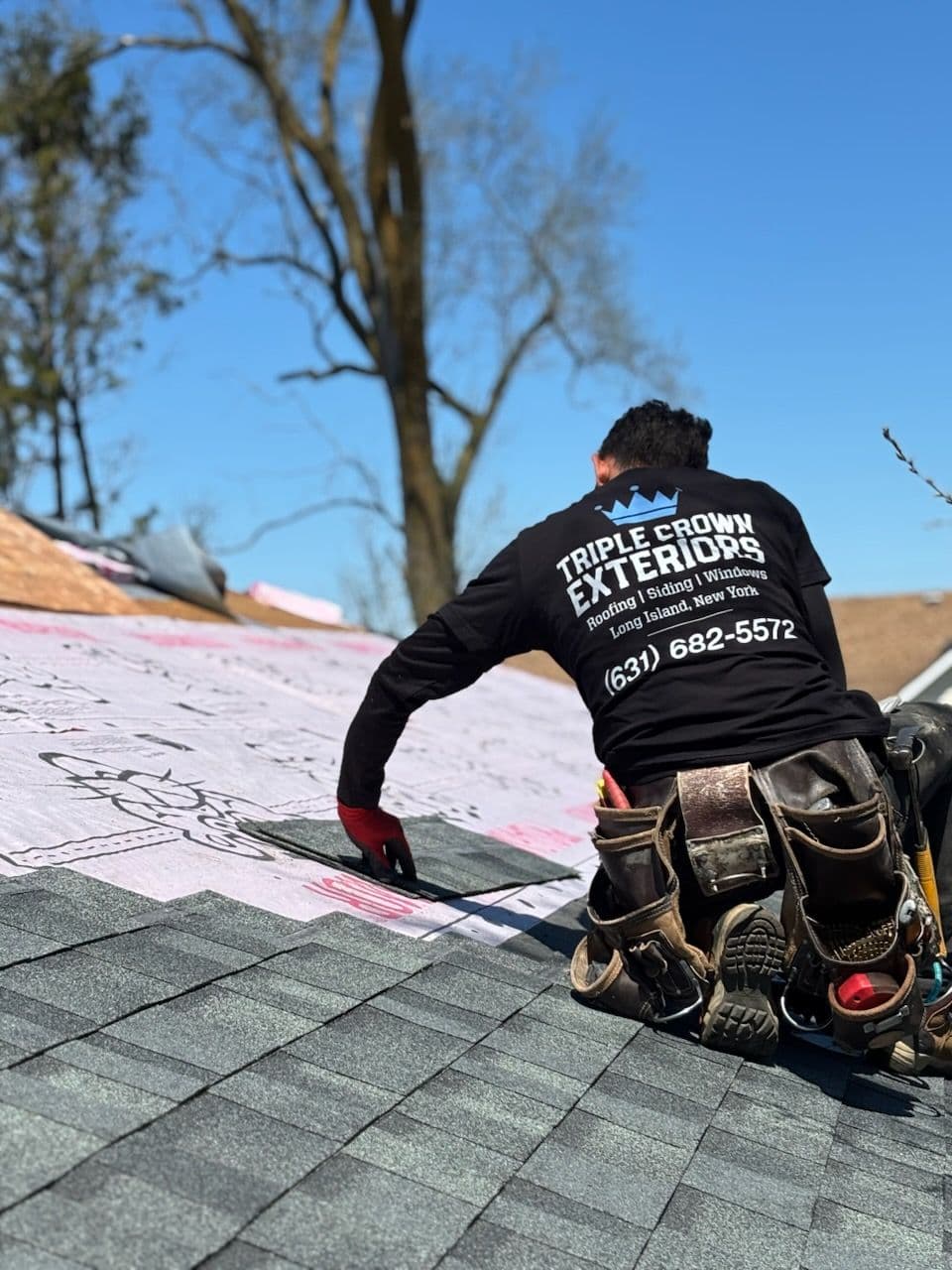 Roofer installing shingles on a house rooftop with professional gear. Triple Crown Exteriors.