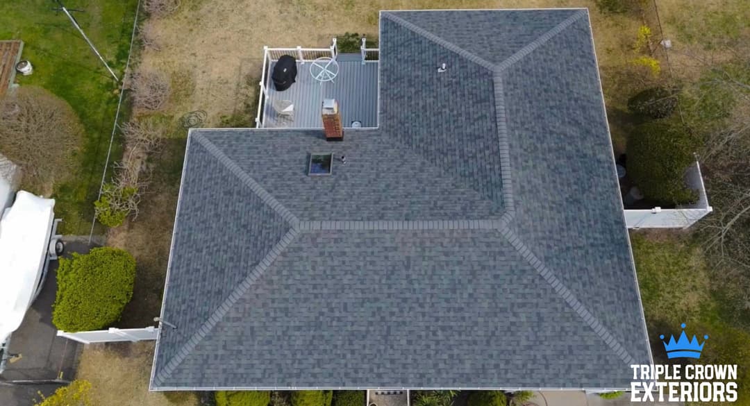 Aerial view of a modern home with a gray shingle roof and surrounding lawn.