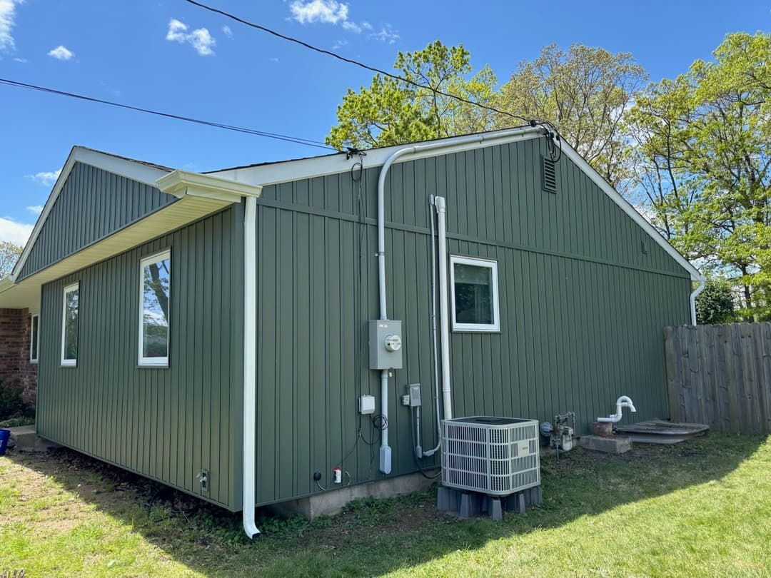 Green-sided house exterior with electrical meter and air conditioning unit on a sunny day.