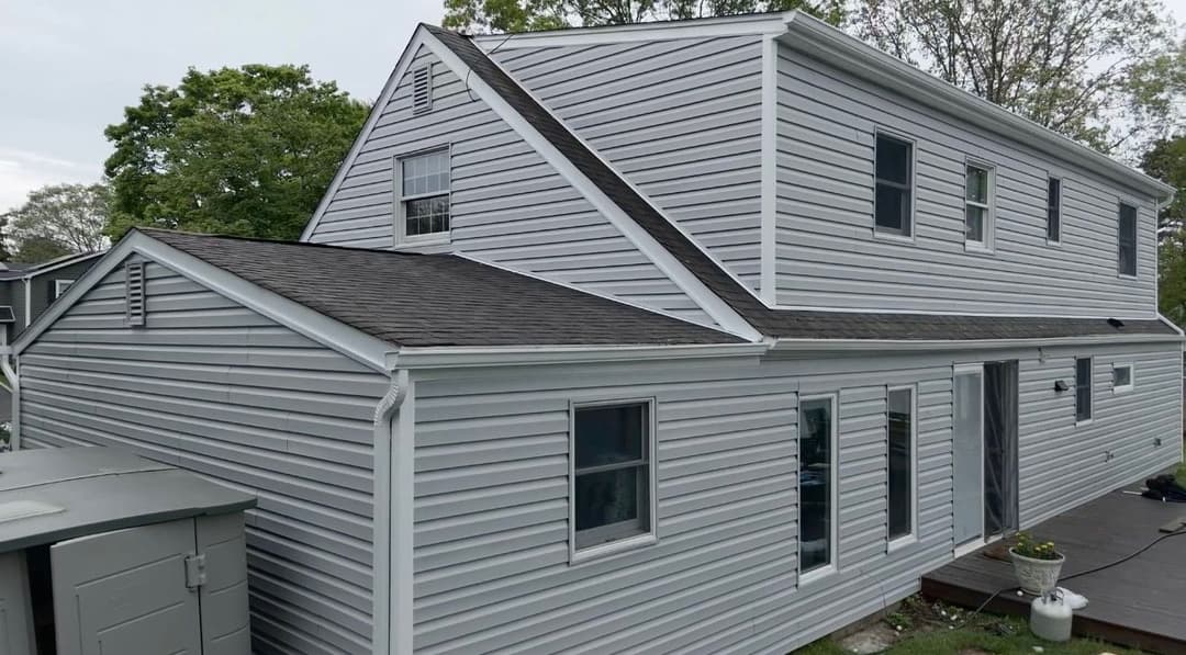 Modern gray house exterior with new siding, featuring large windows and a backyard deck.