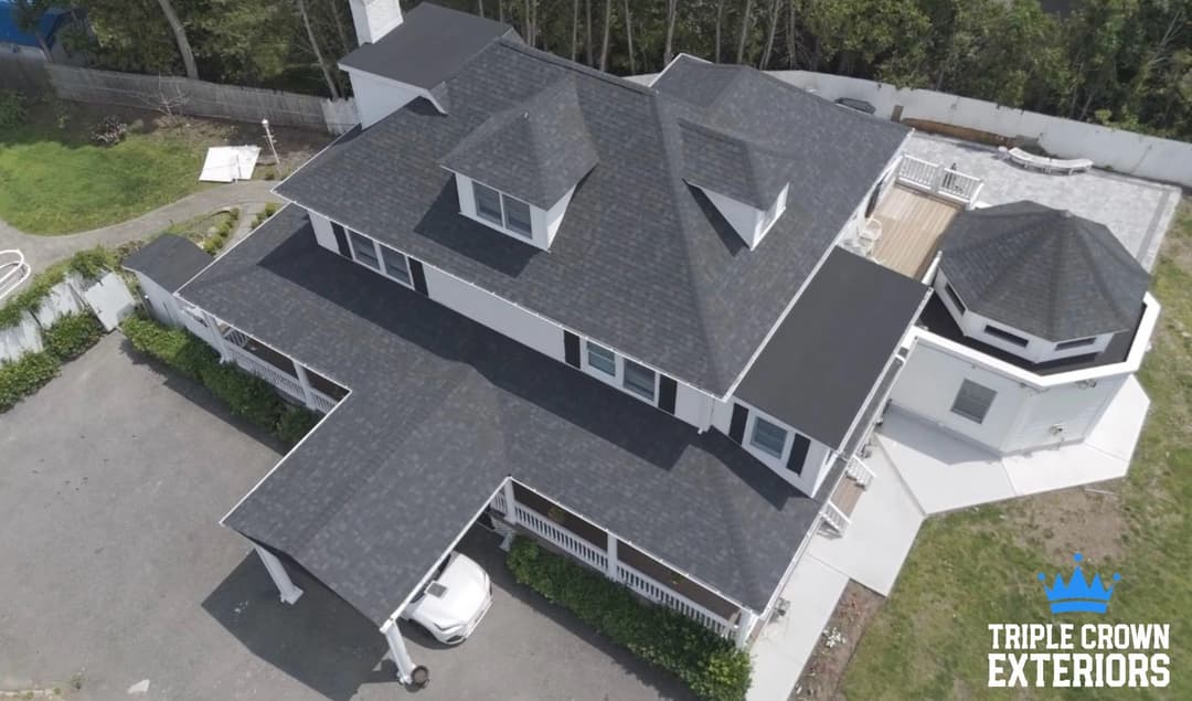 Aerial view of a large modern home with a black roof and white exterior by Triple Crown Exteriors.