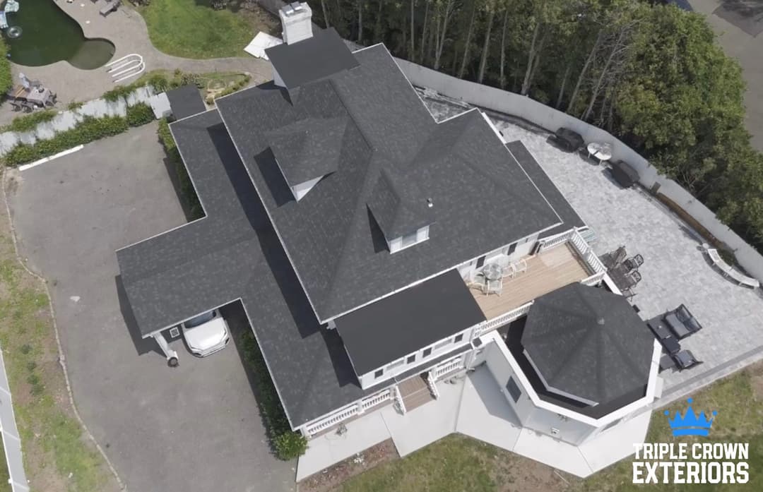 Aerial view of a modern home with a large deck and stylish roof design. Triple Crown Exteriors logo.