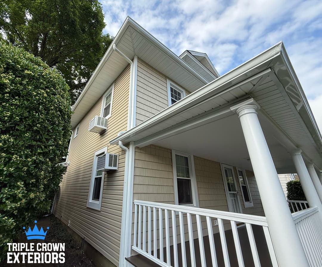 Modern home exterior featuring beige siding, white porch, and air conditioning units. Triple Crown Exteriors.