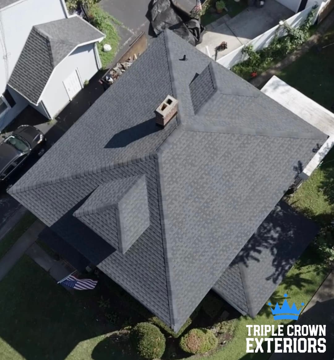 Aerial view of a modern home with a dark shingle roof and chimney, showcasing exterior features.