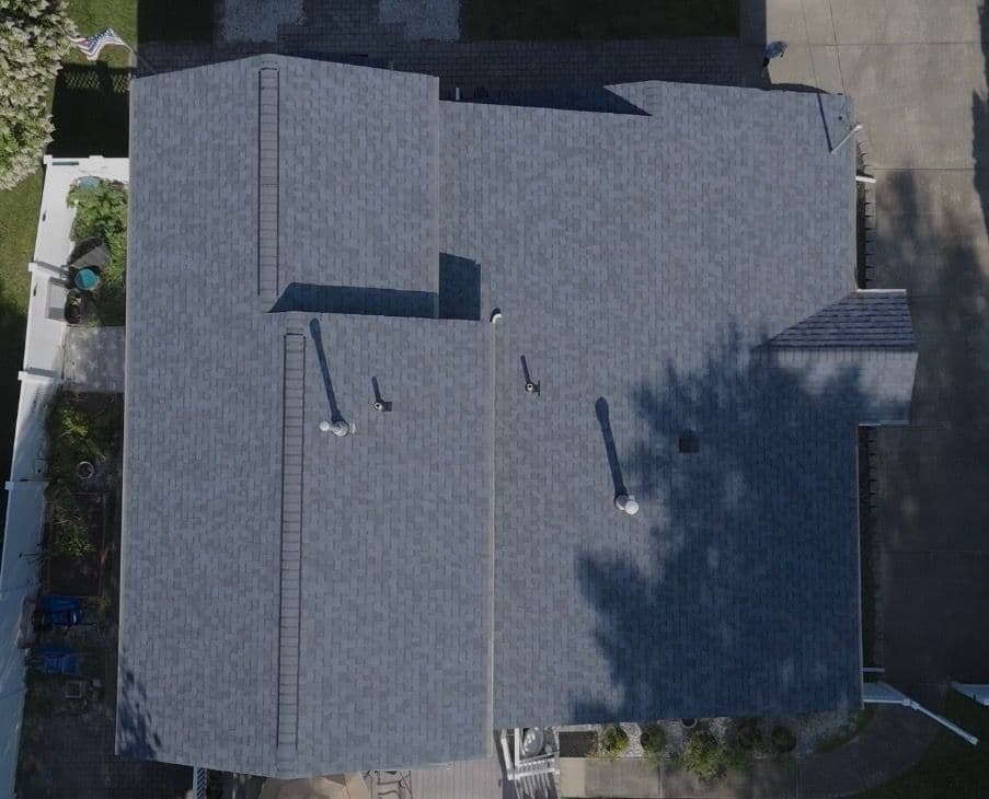 Aerial view of a modern home with a dark gray shingle roof and outdoor features visible.