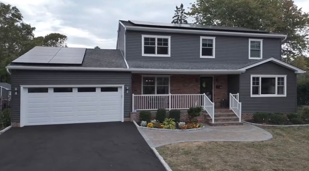 Modern gray house with solar panels, front porch, and landscaped yard in suburban setting.
