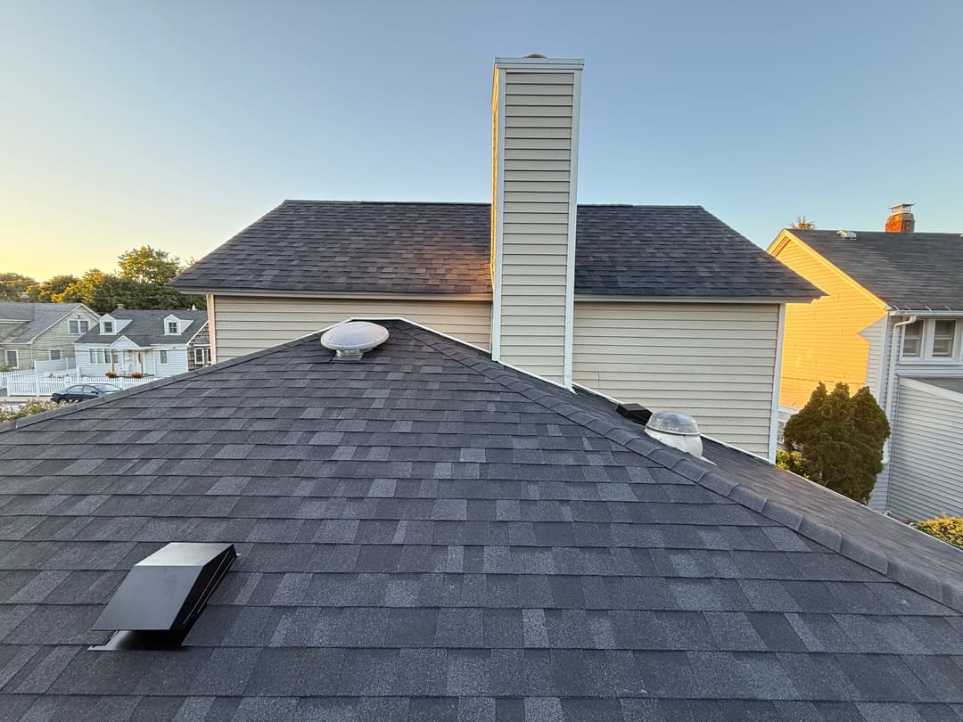View of a sloped roof with vents and a chimney against a clear sky at sunset.